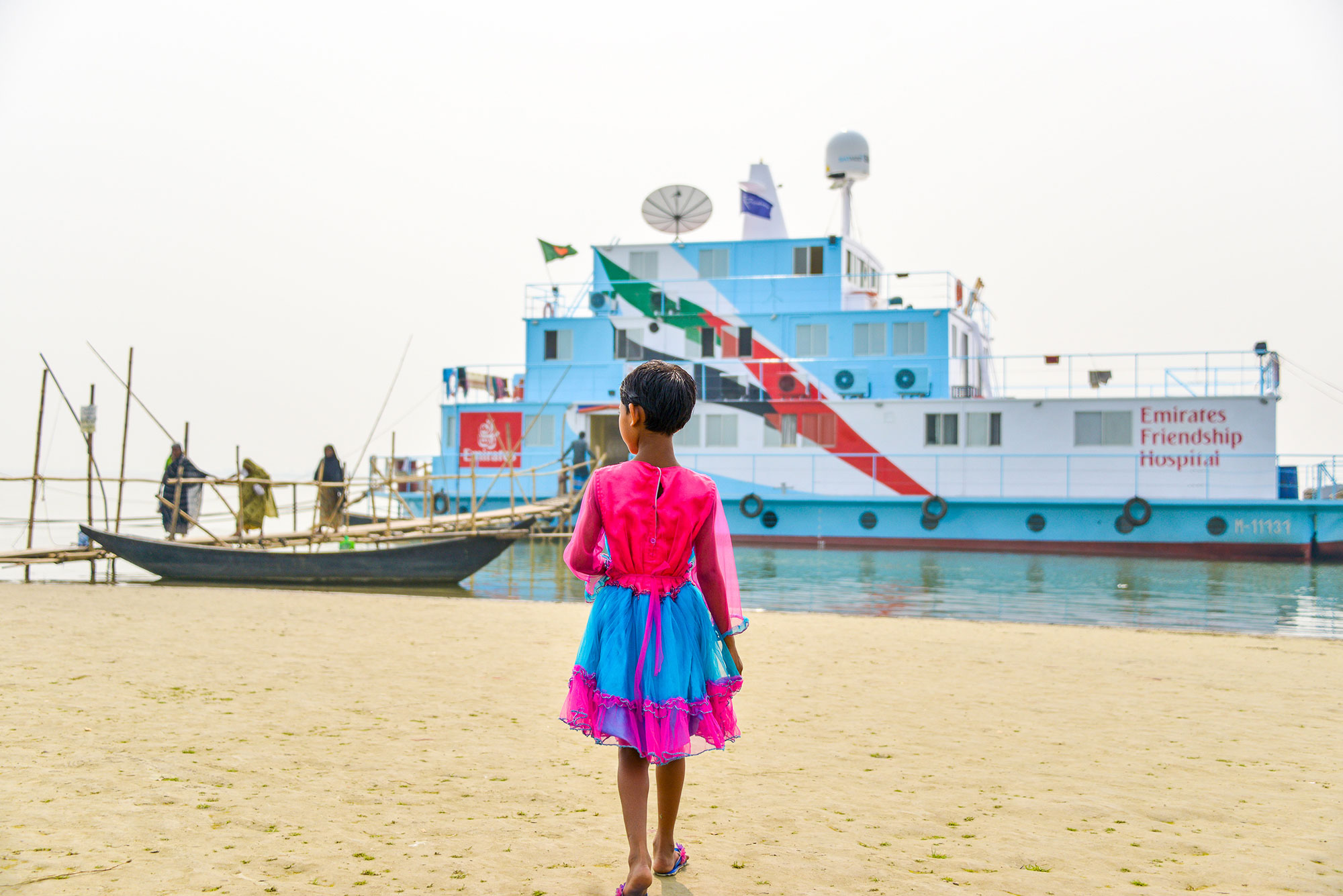 Girl in pink dress standing in front of Emirates Friendship Hospital ship