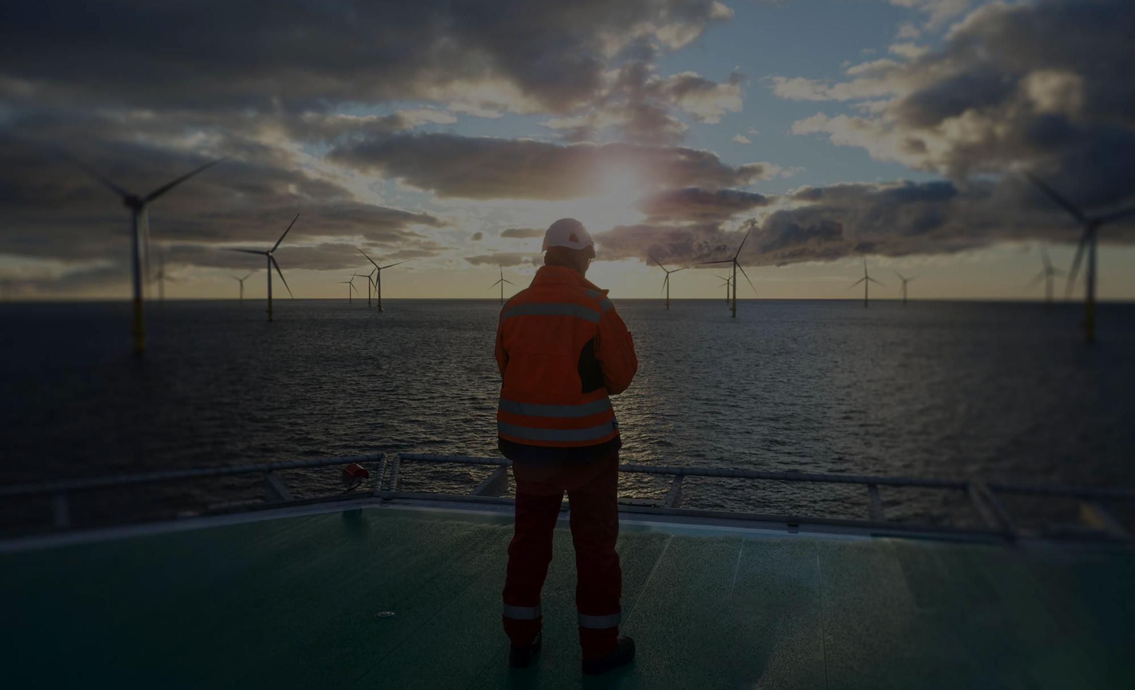 Man standing on remote platform overlooking wind turbines