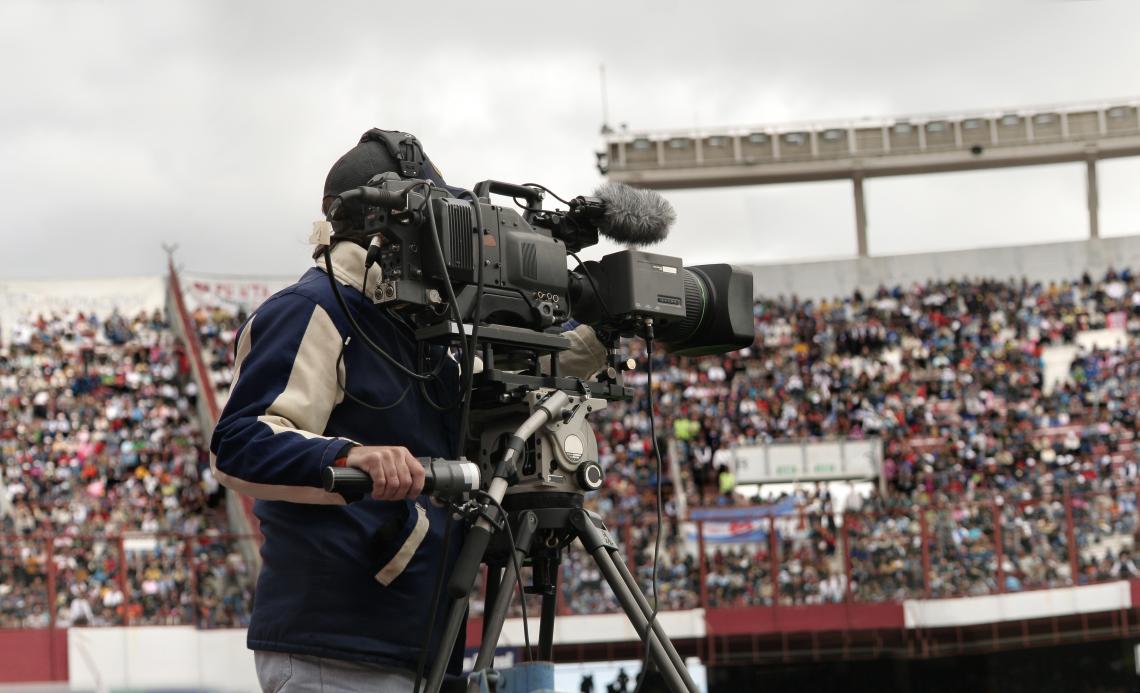 A cameraman films a sports event in a packed stadium.