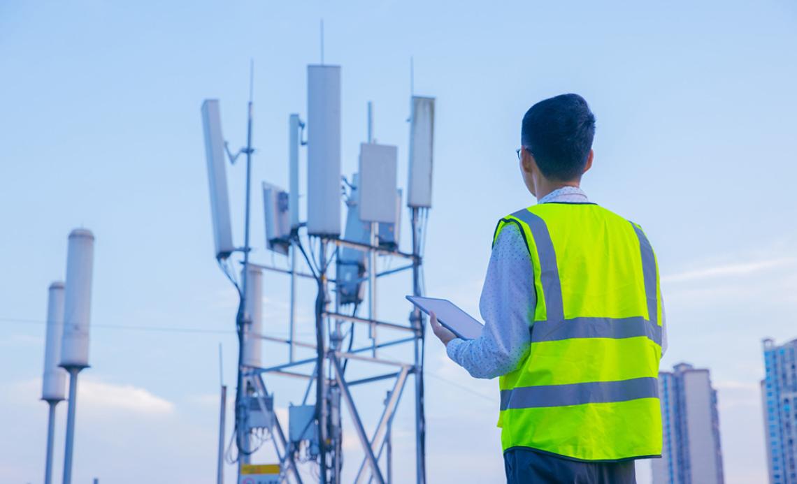 Image of technician in a safety vest inspecting a cellular tower