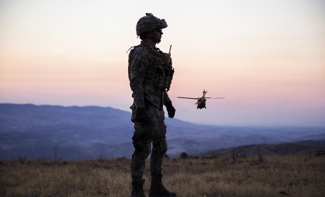 Image of a soldier on open terrain with a helicopter behind.
