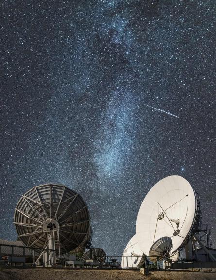 Antenna dishes on land at night while many stars are visible