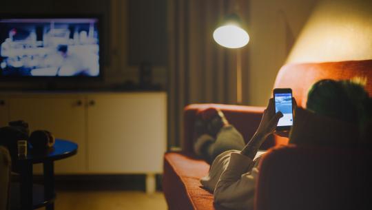 Woman on couch watching tv with phone