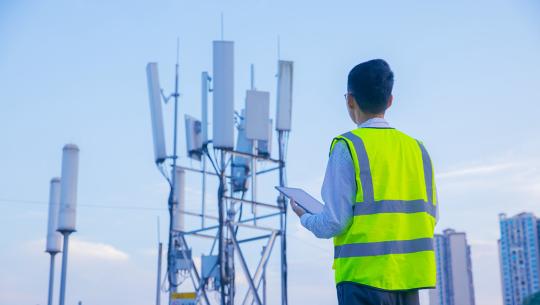 Image of technician in a safety vest inspecting a cellular tower