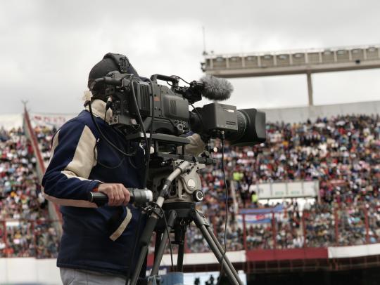 A cameraman films a sports event in a packed stadium.