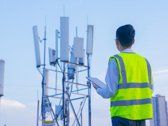 Image of technician in a safety vest inspecting a cellular tower