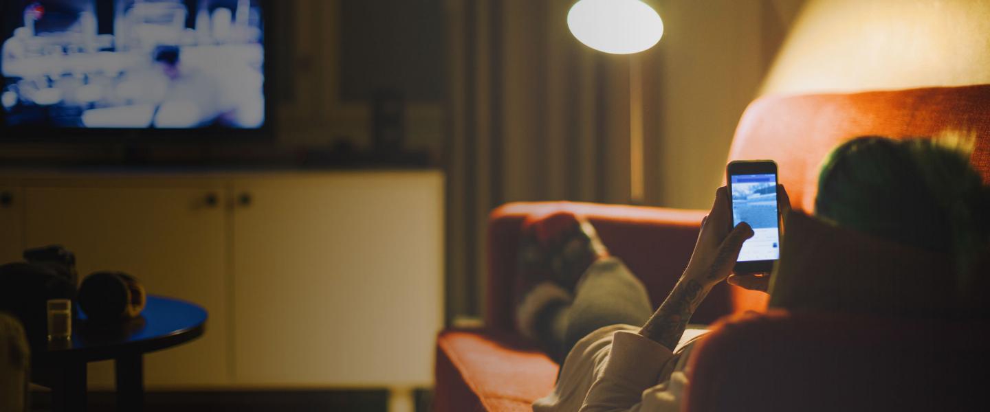 Woman on couch watching tv with phone