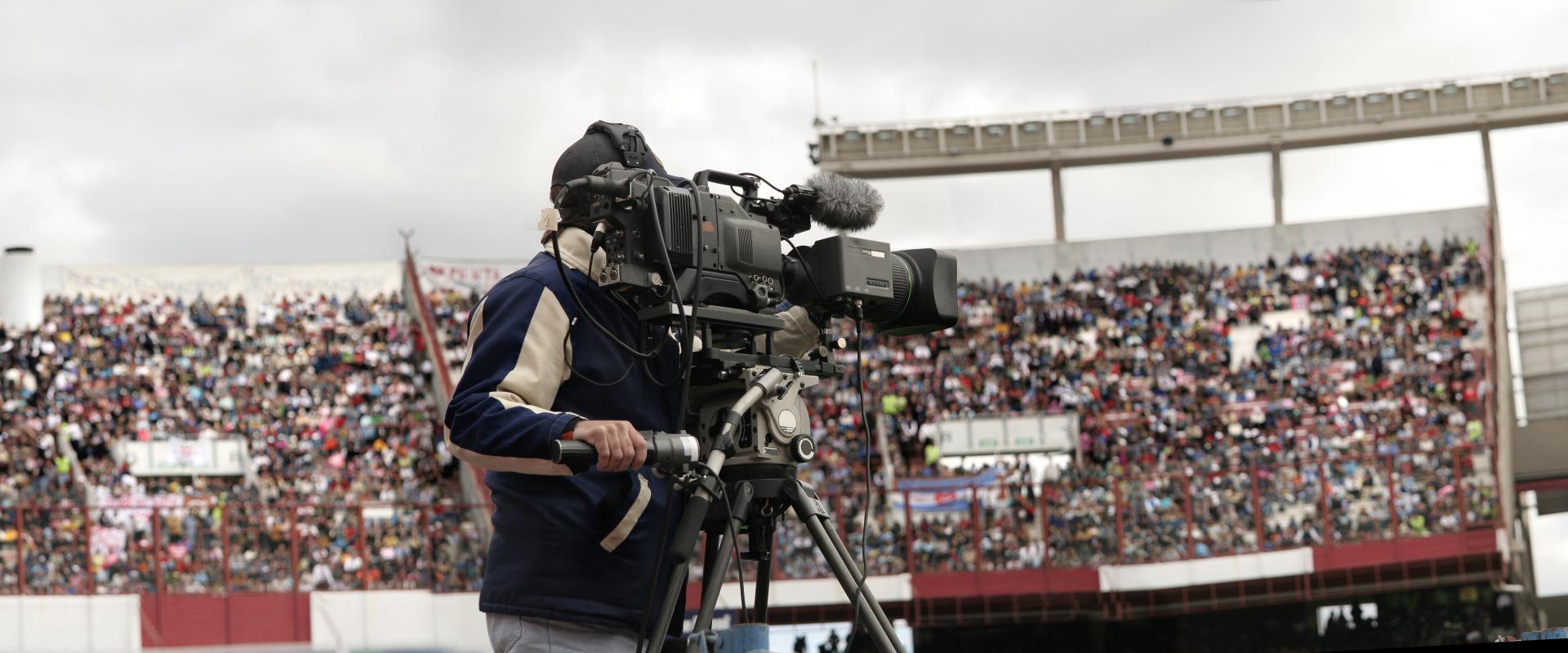 A cameraman films a sports event in a packed stadium.