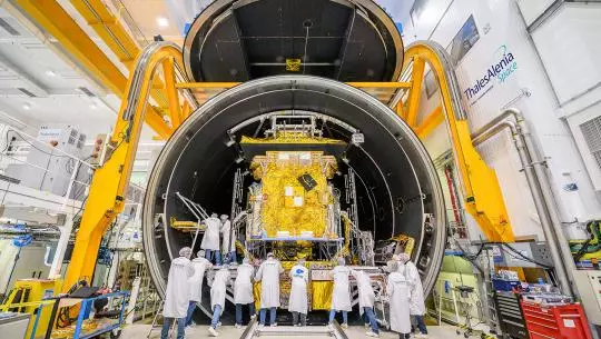 Engineers preparing a satellite inside a large testing chamber.