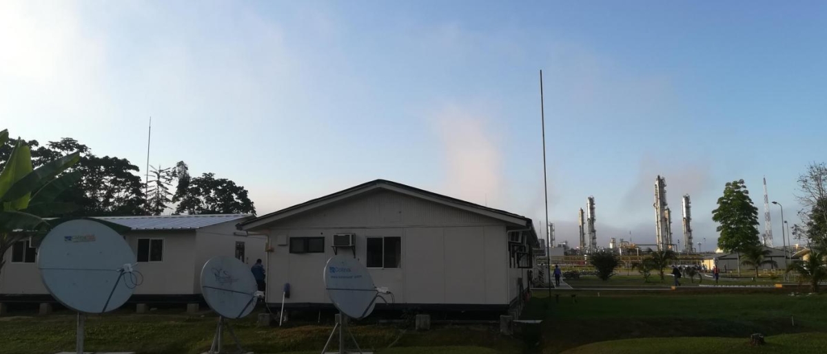 Image of satellite dishes outside small buildings near an industrial facility.