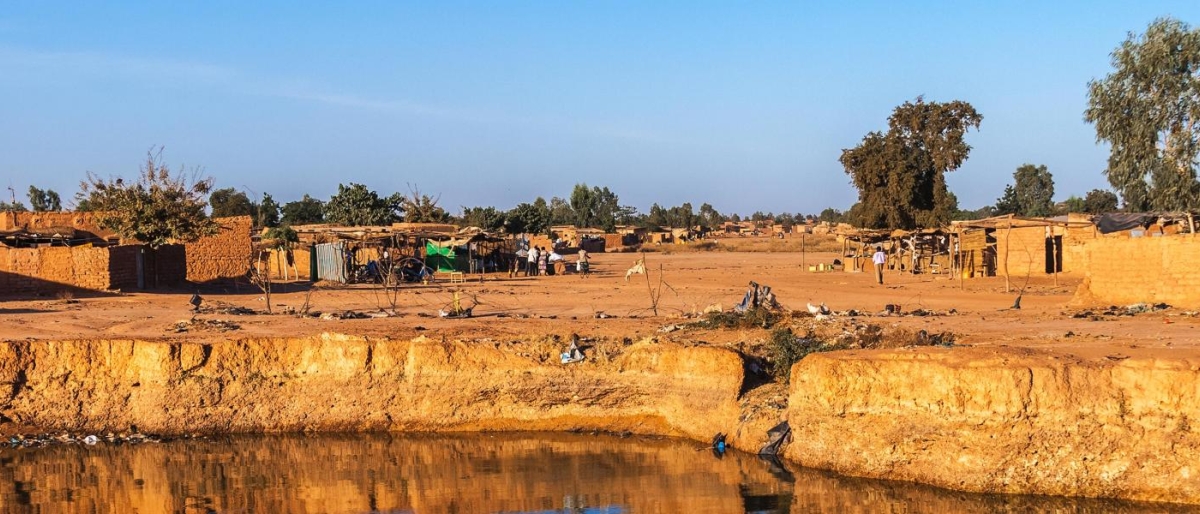 Image of a rural desert village with small clay structures and a water channel in the foreground