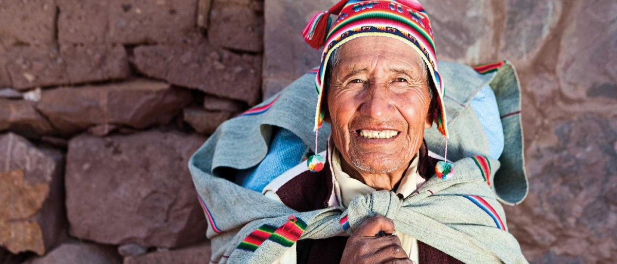 Image of a person in traditional woven clothing standing against a stone wall.