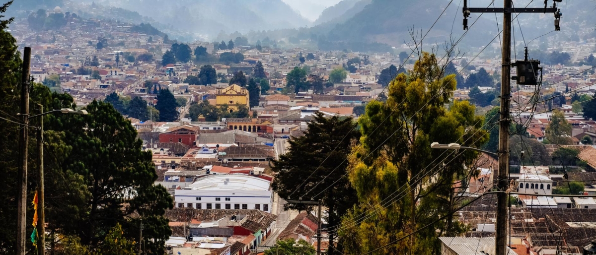 Landscape image of hillside view overlooking a dense town surrounded by mountains and trees.