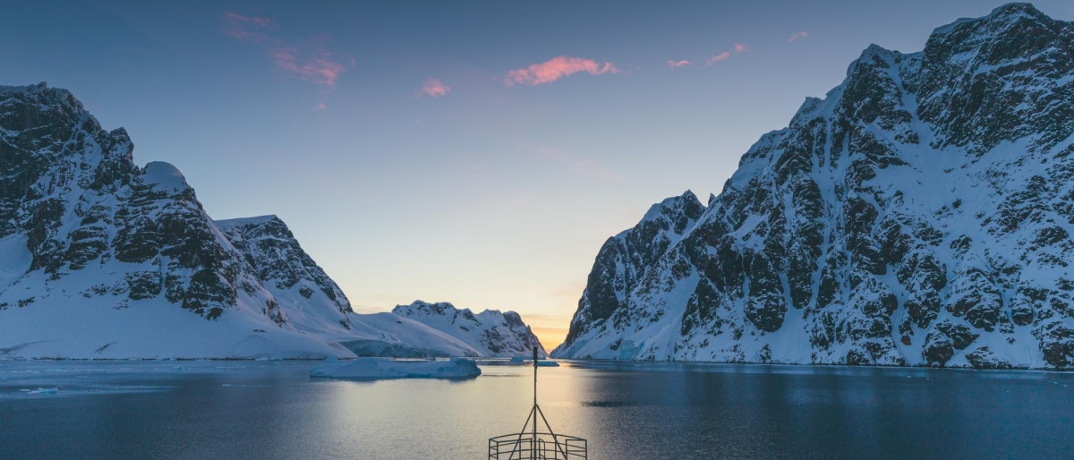 Image of a Ship cruising through icy fjord at sunset between snow-covered mountains