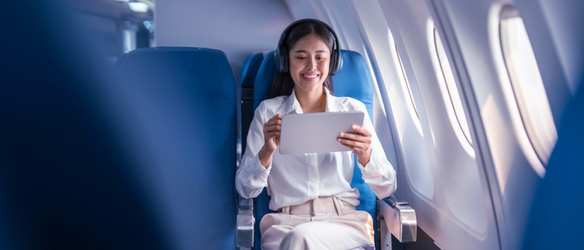 Image of a woman wearing headphones using a tablet inside an airplane