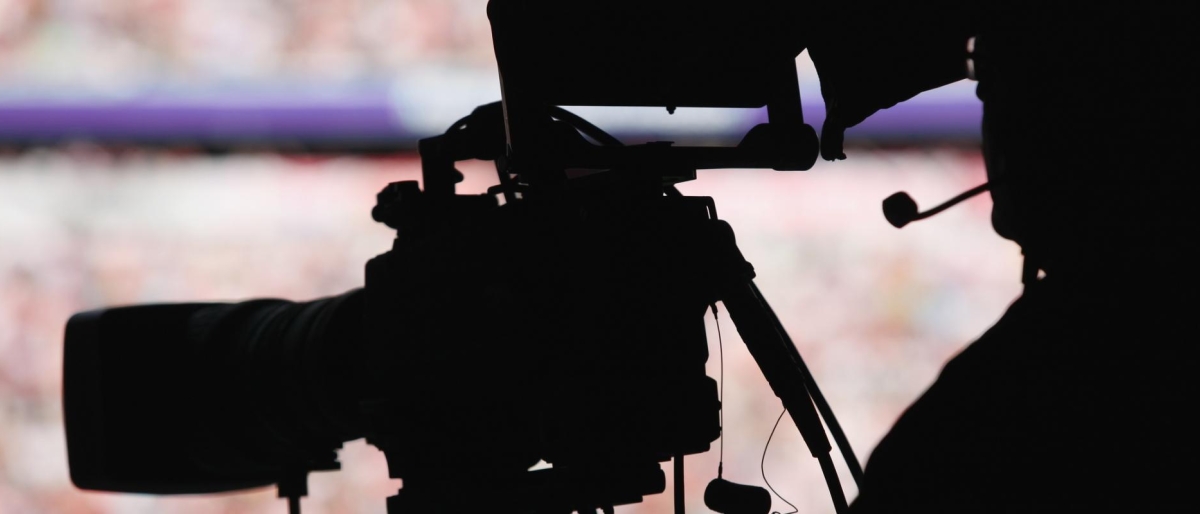 Image of silhouette of a camera operator filming with a broadcast camera.