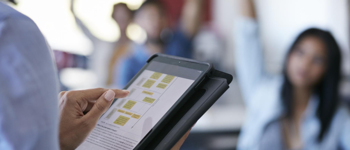 Image of a person holding a tablet displaying a flowchart in a classroom setting.