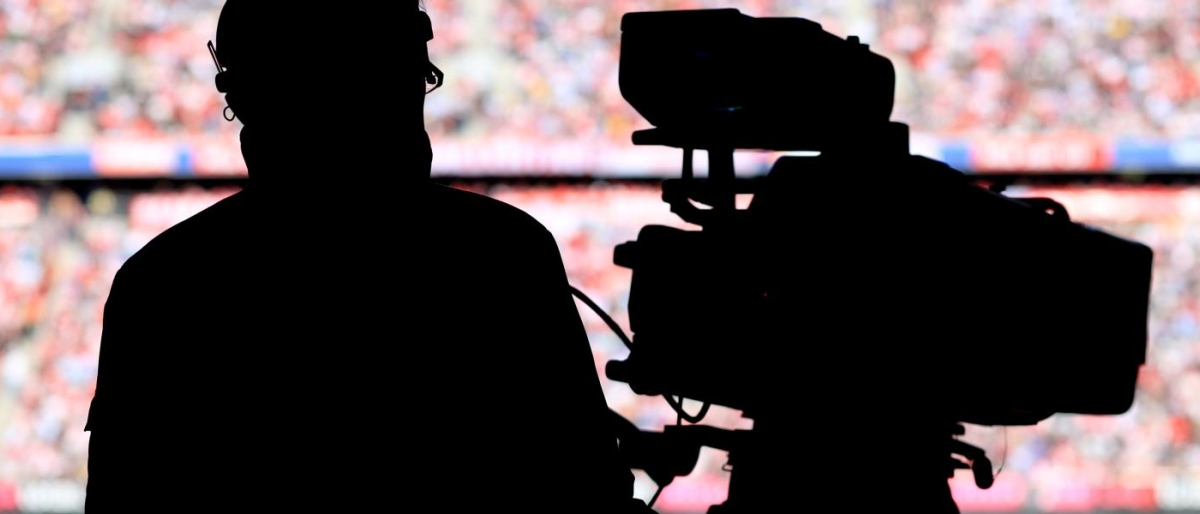 Image of a camera operator's silhouette filming with a broadcast camera.