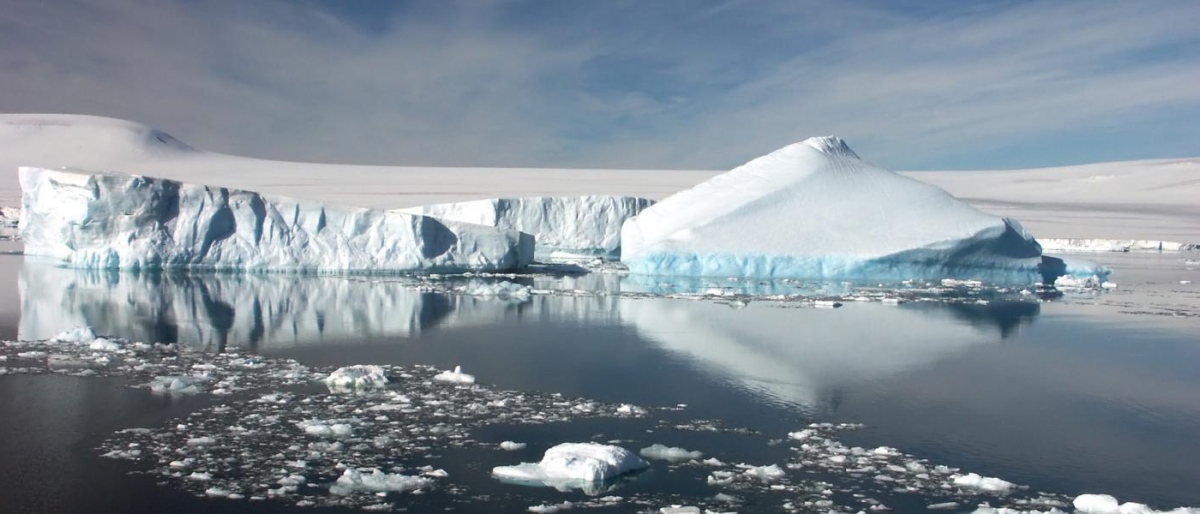 Landscape image of a large iceberg reflecting on calm Arctic water.