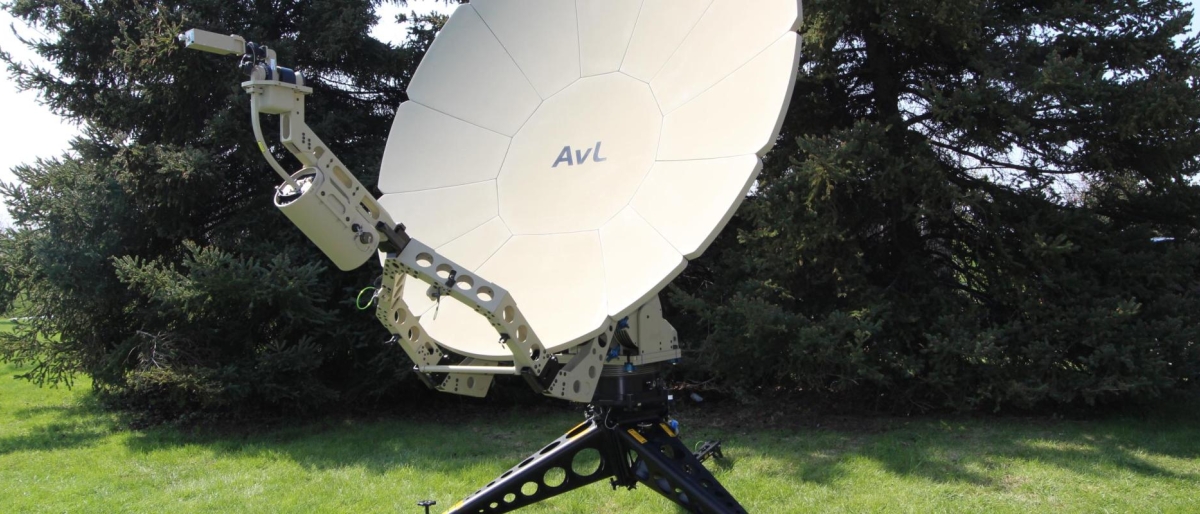 Image of a satellite dish on a lawn with bushes in the background.