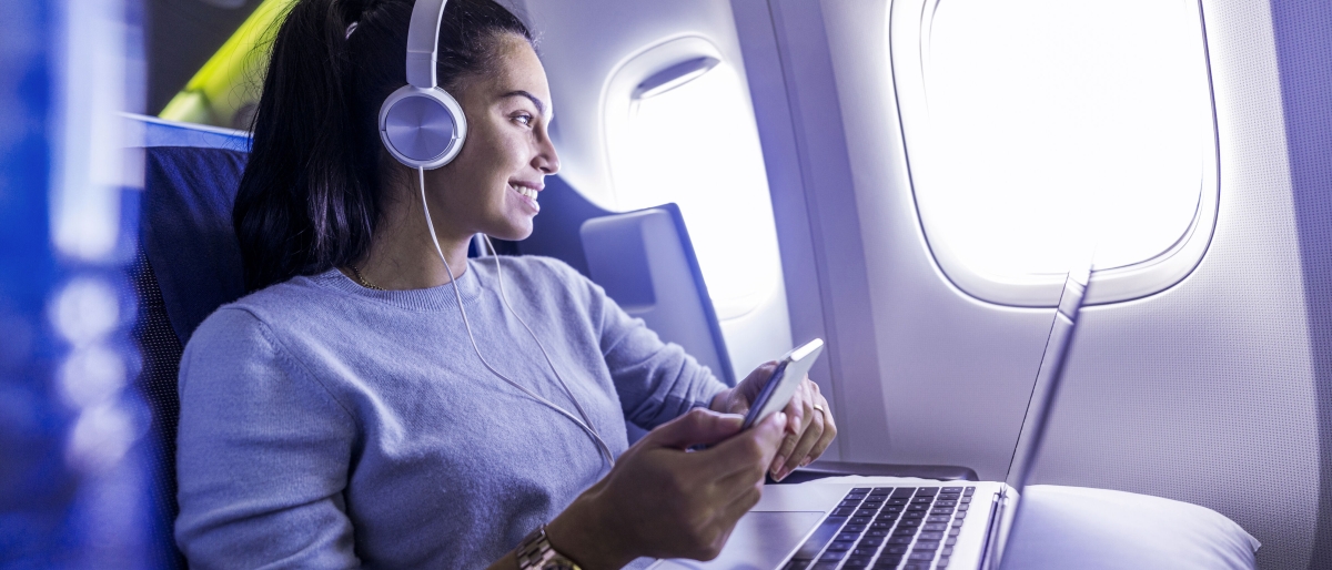 Image of a person inside an airplane using mobile phone and laptop.
