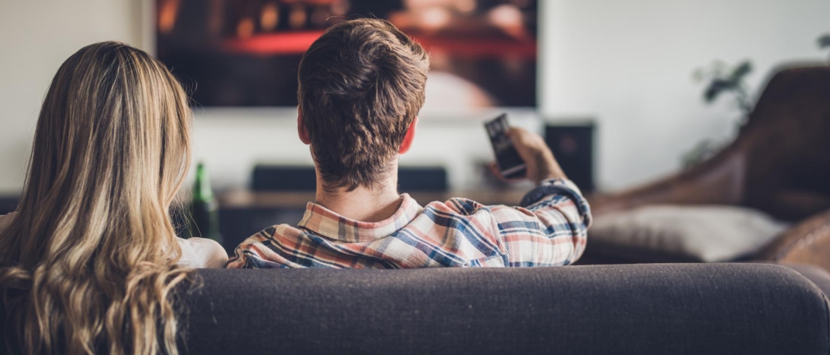 Image of two people on the couch watching television.