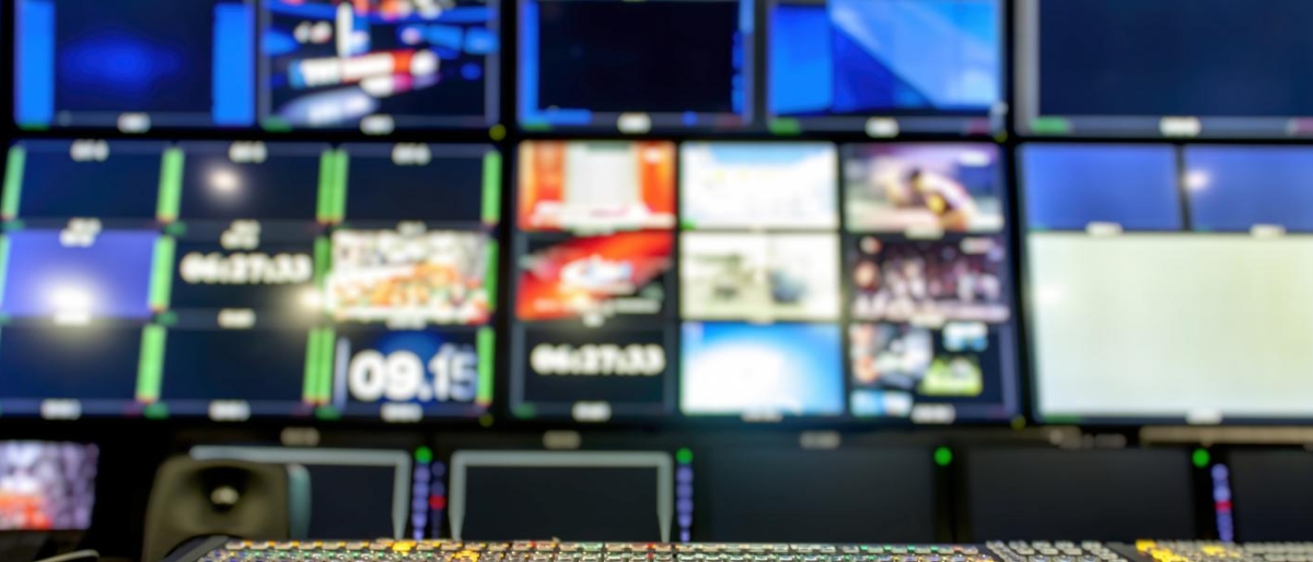 Broadcast control room with a switcher panel and multiple screens.