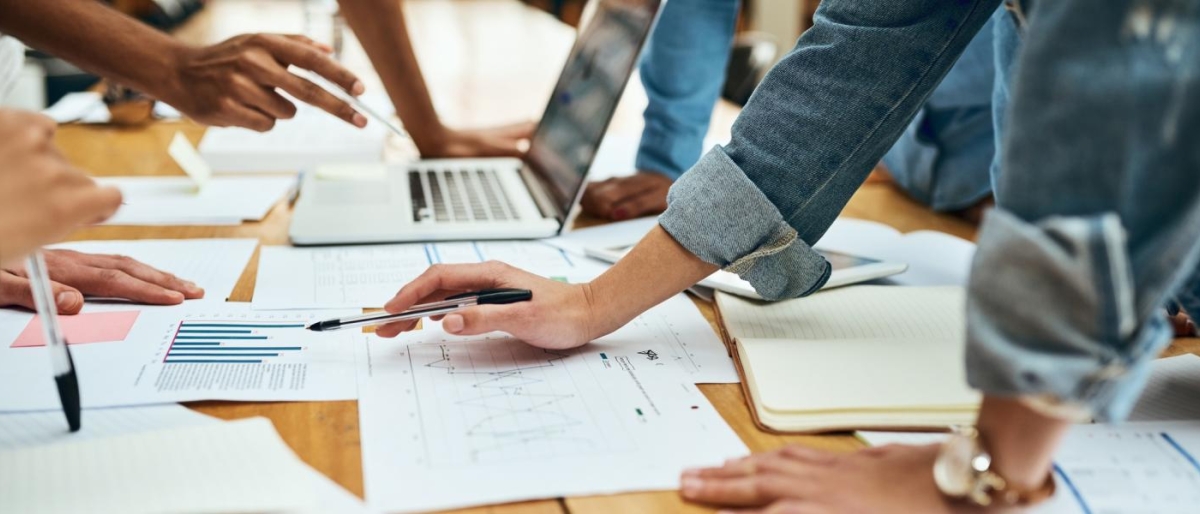 Closeup image of employees working at a table with laptops, papers and pens