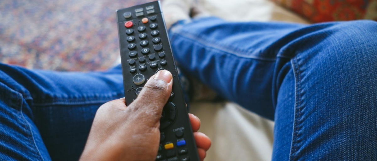 Close‑up image of a hand holding a TV remote while seated.