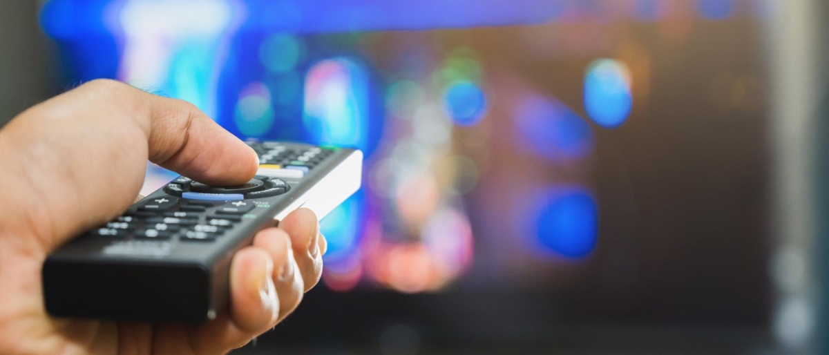 Image of hand holding a TV remote pointed at a colorful screen.