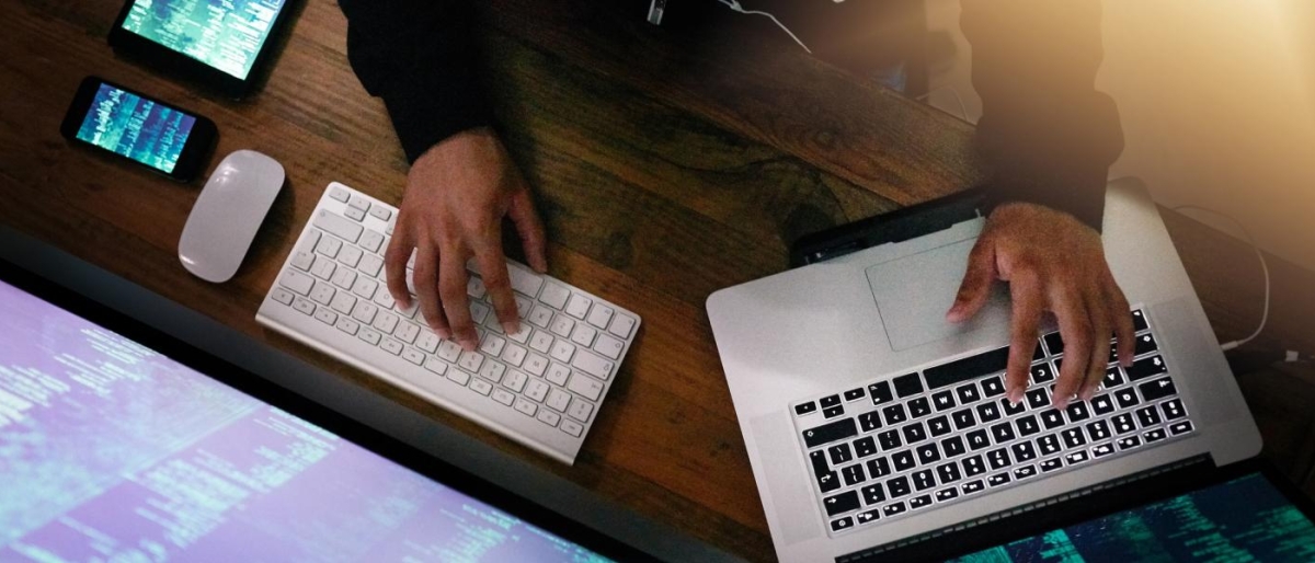 Image of close-up a person working with a laptop, keyboard and monitor.
