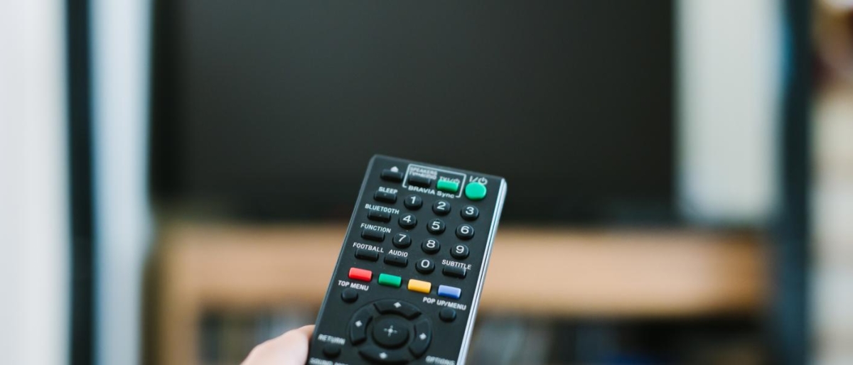 Closeup image of a person holding a remote in front of television.