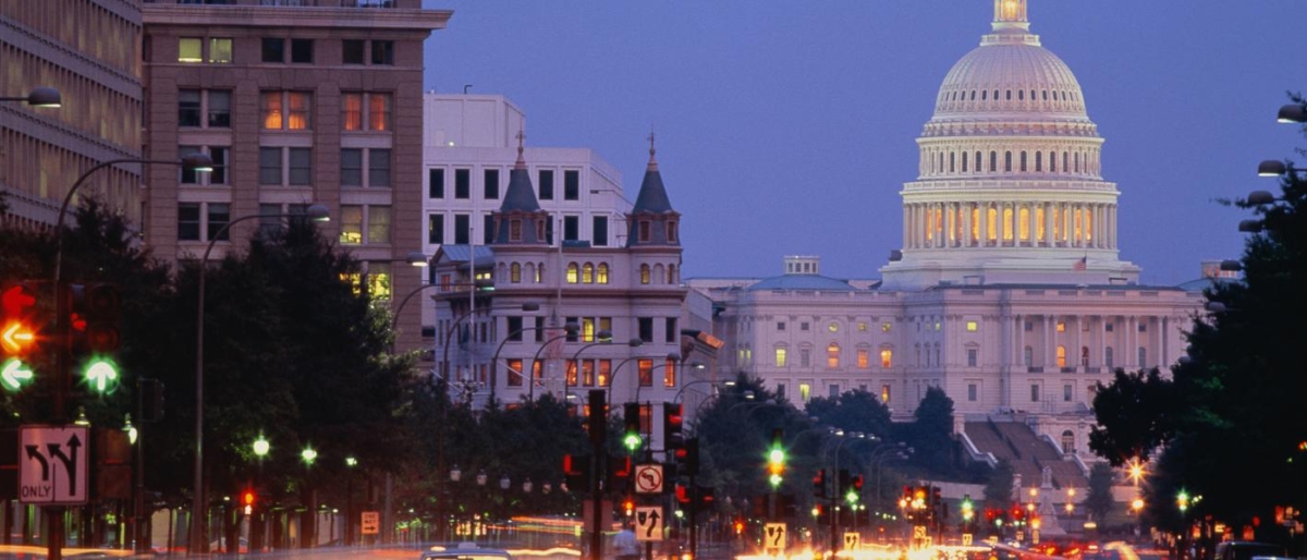 Image of a night view of a city street leading to a brightly lit building.