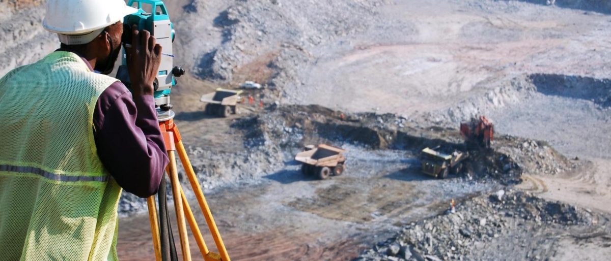 Image of a surveyor using measurement equipment overlooking an open‑pit mining site.