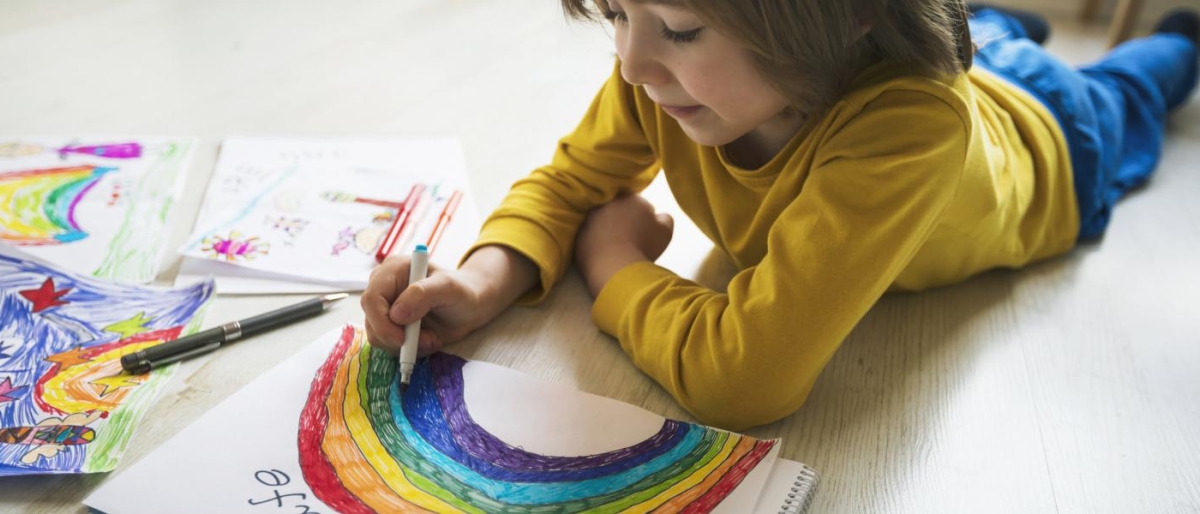 Image of a kid drawing a colourful rainbow.
