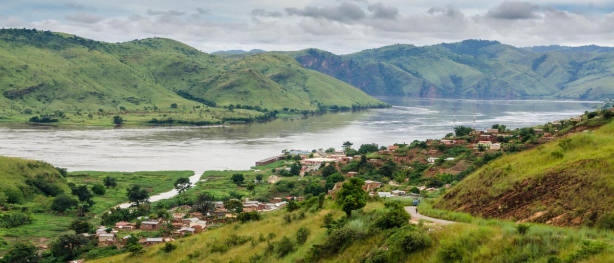 Landscape image of a riverside village with green hills and a wide river.