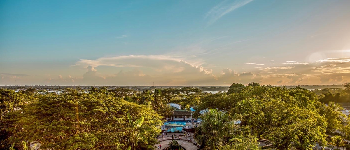 Image of a tropical town surrounded by lush green trees under a warm sunset sky.