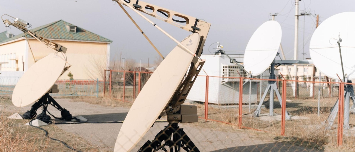 Portable tan satellite dishes set up outdoors near fixed white antennas