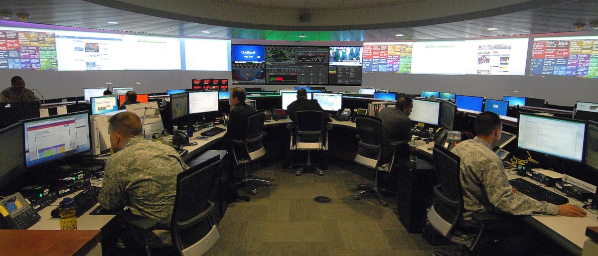 Image of military-style command center with personnel monitoring multiple screens.