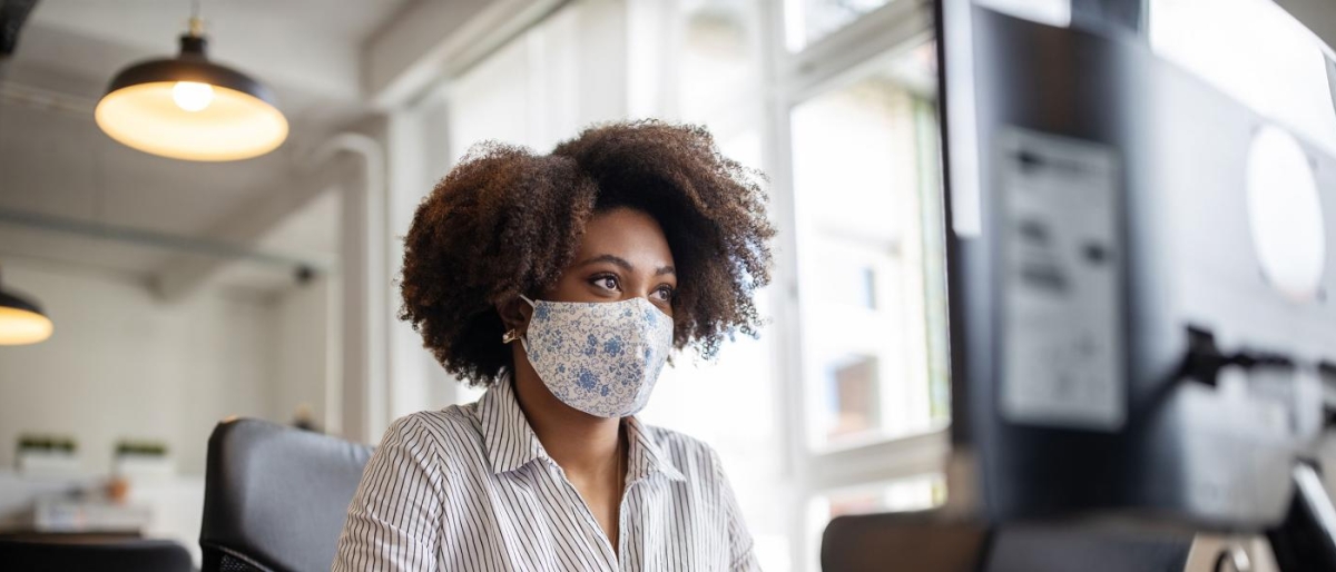 Image of a person wearing mask looking at a computer screen.