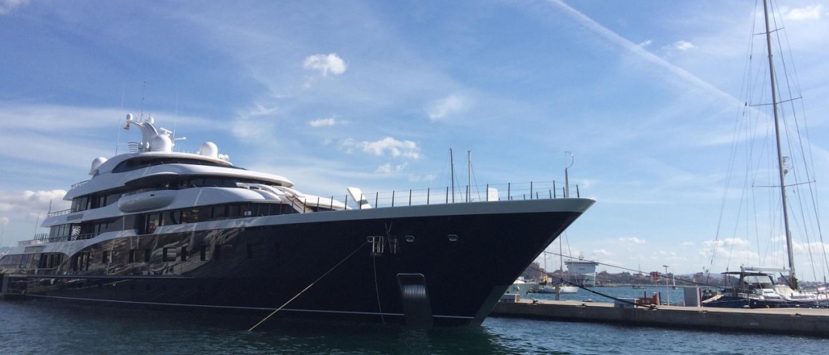 Image of a large luxury yacht docked at a marina under a clear sky.