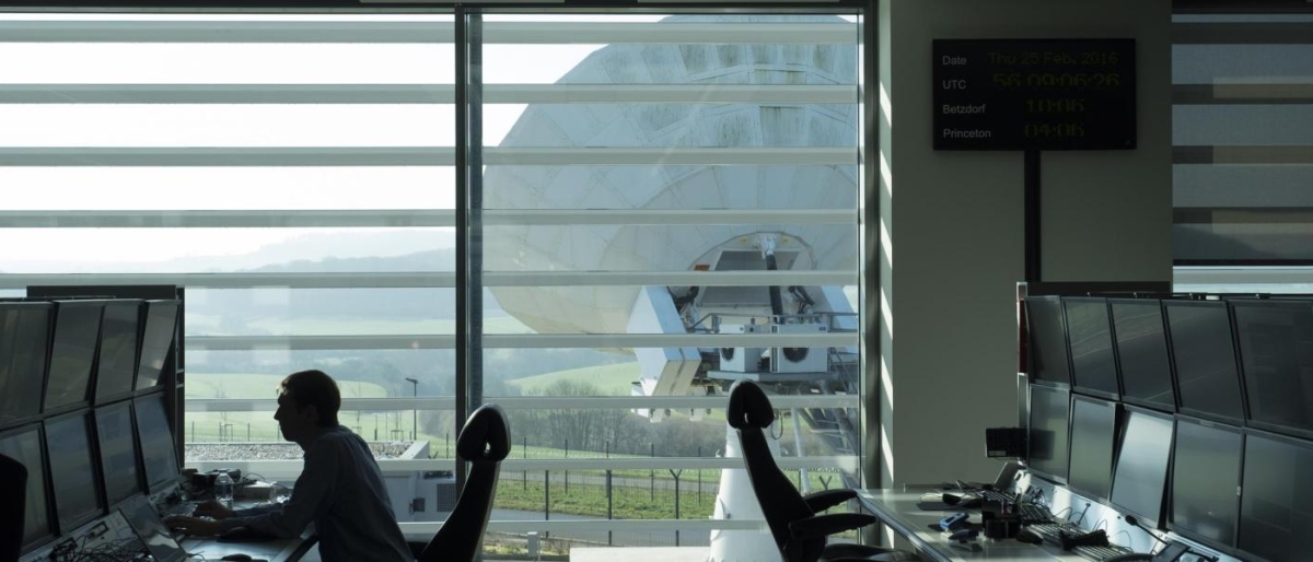 Image of control room monitors facing a large satellite dish outside
