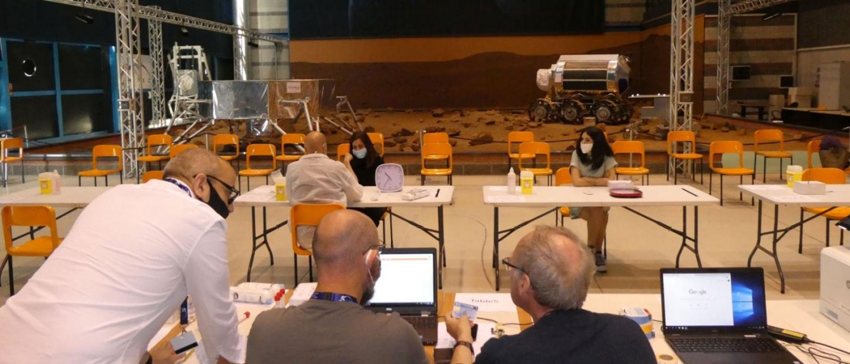 Team working at tables with laptops featuring space‑rover equipment.