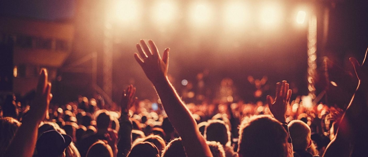 Image of people at a concert raising their hands toward a brightly lit stage.