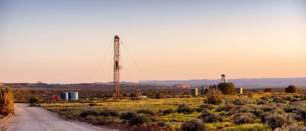Image of a landscape with a tall drilling rig and storage tanks.