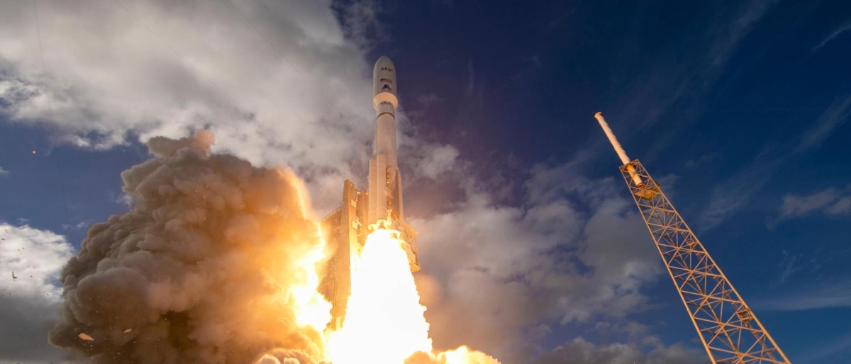 Image of rocket lifting off with bright exhaust flames against a cloudy sky.