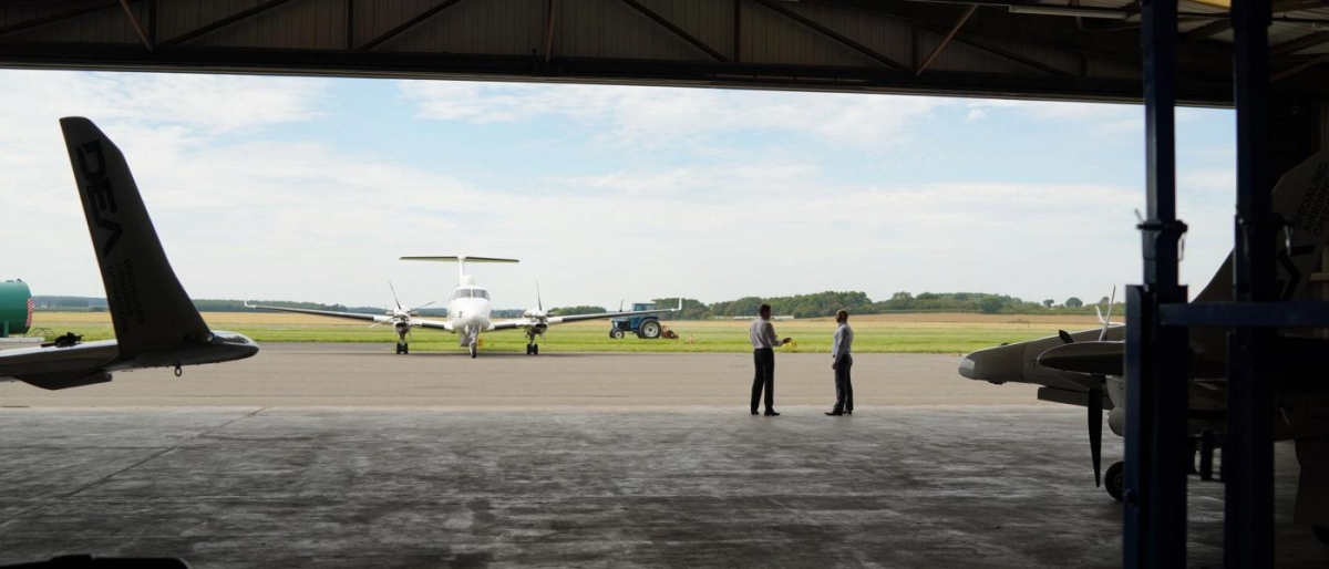 Image of a plane in an aerodrome and two people next to it.