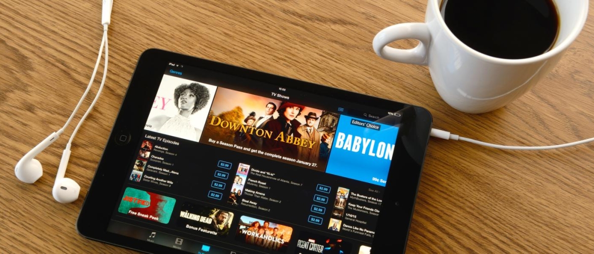 Image of tablet showing TV shows next to earbuds and a cup of coffee.