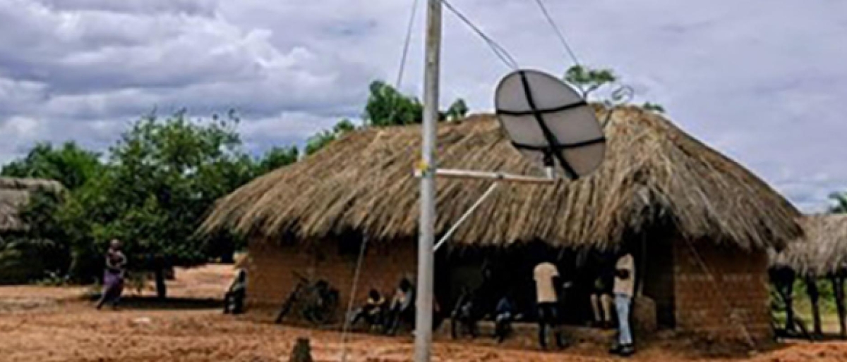 A satellite dish beside a thatched-roof building in a rural area.