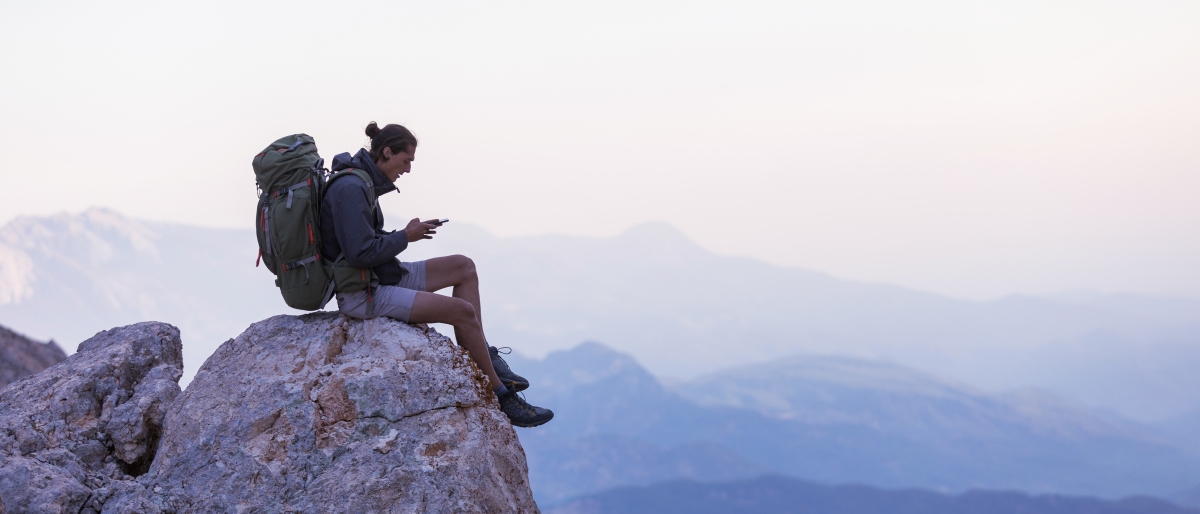 Hiker sitting on a mountain peak using a phone.